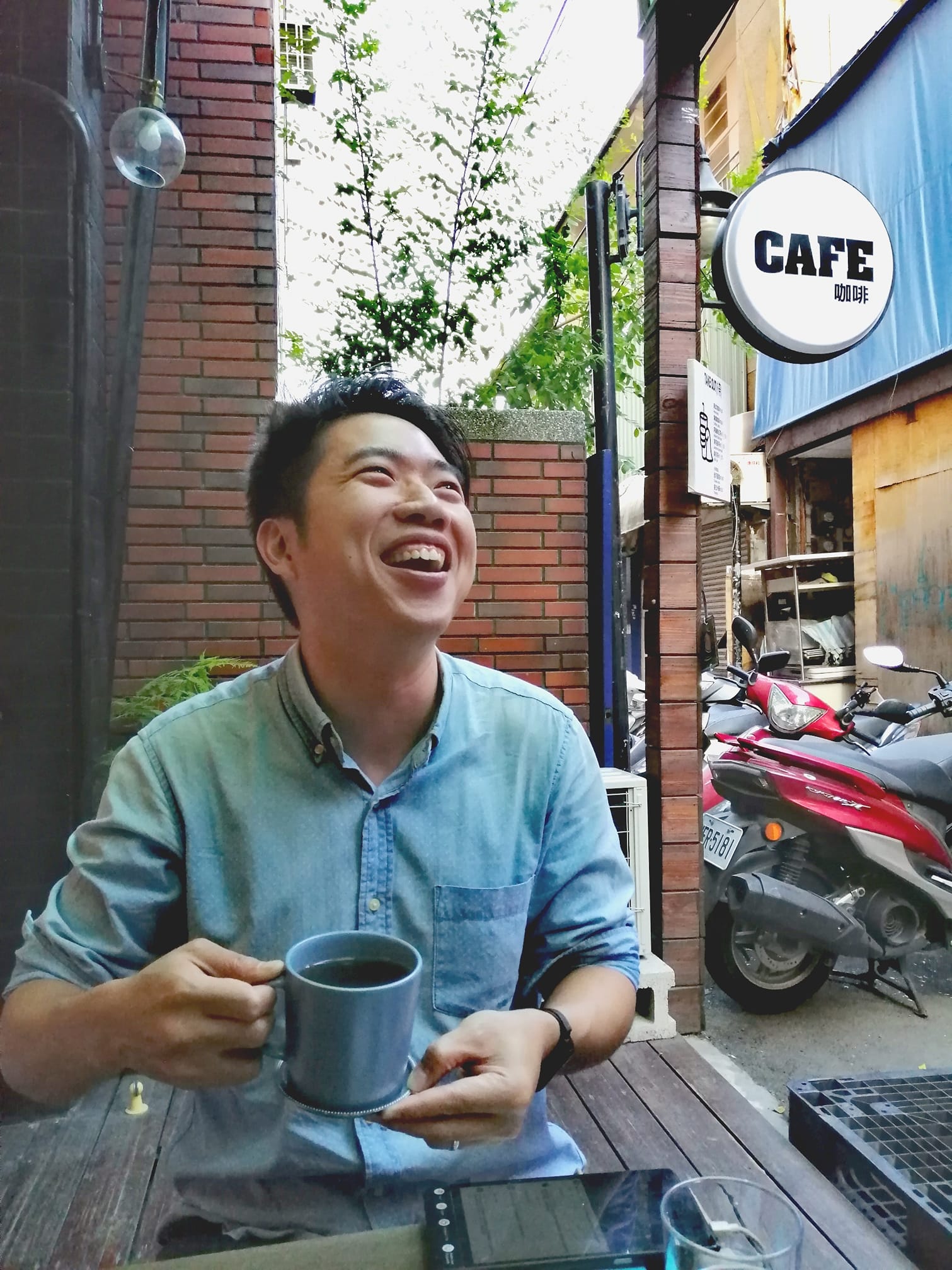 Damien Lee smiling with a cup of coffee at a café